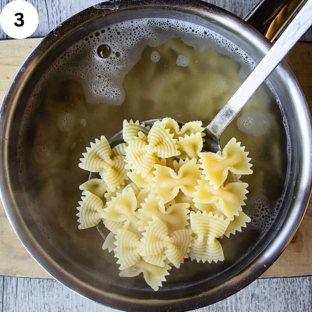 Cooked butterfly pasta in slotted spoon above pot of water.