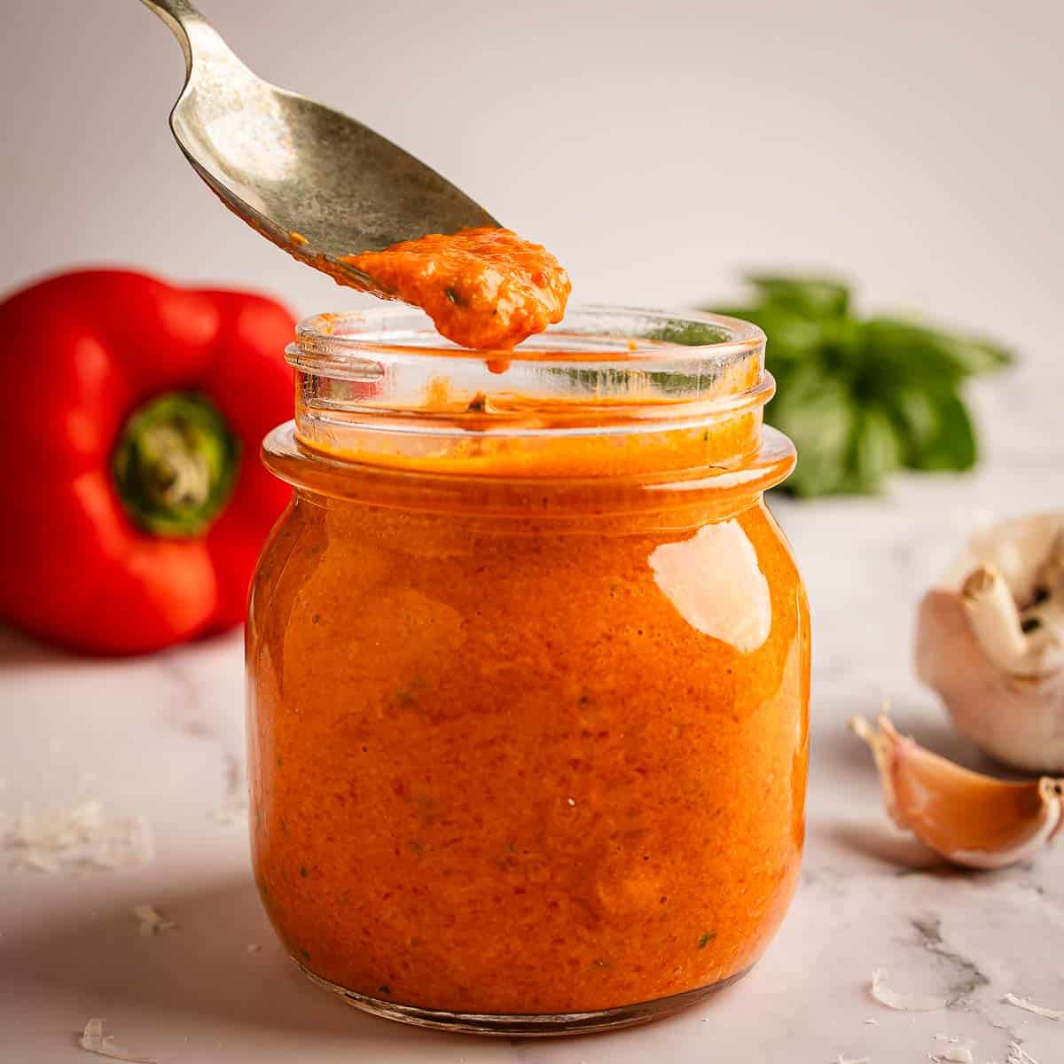 Jar of roasted red pepper sauce with a spoon taking a scoop.