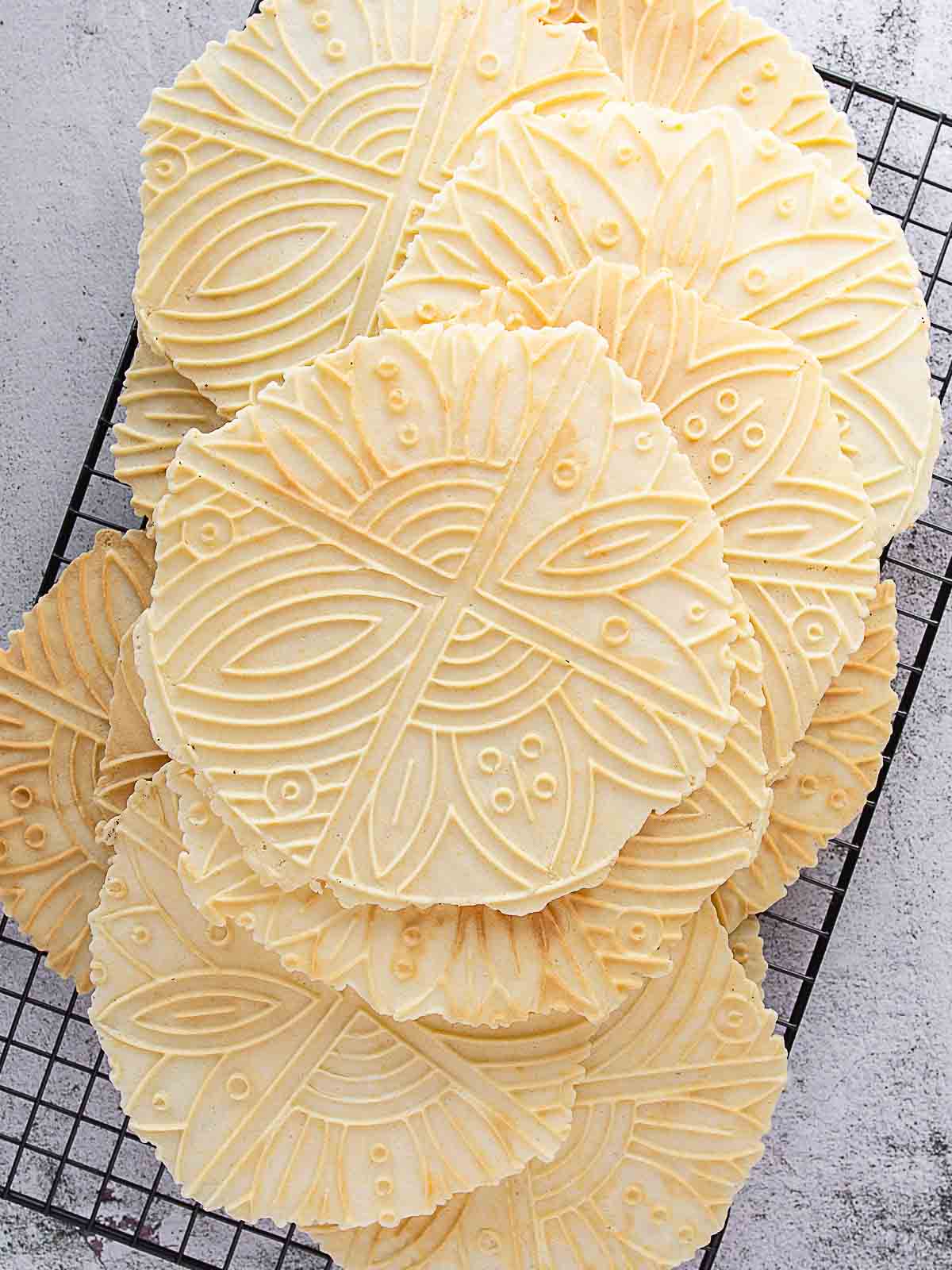 Overhead view of large pizzelle cookies on a wire rack.