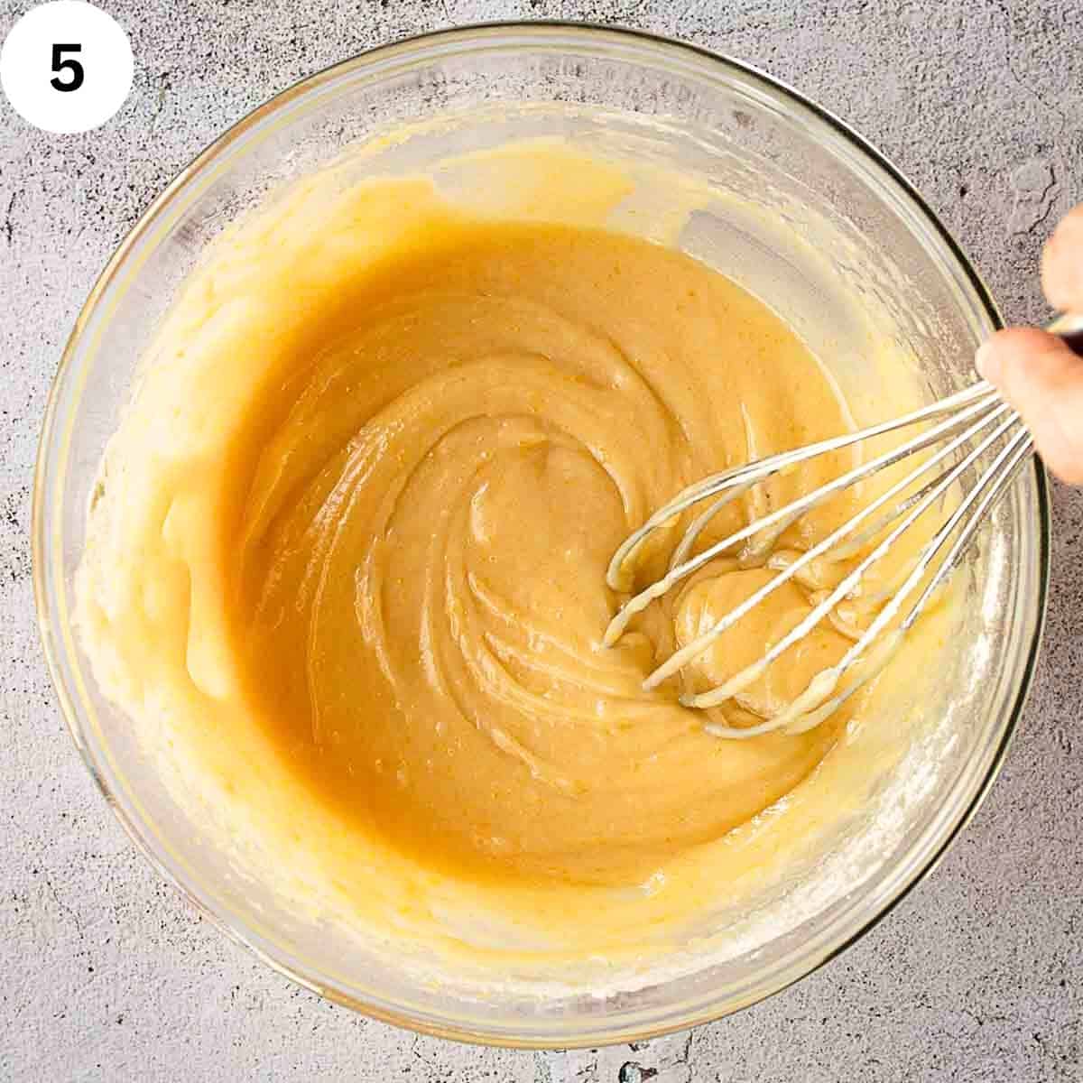 A hand whisk mixing a cake batter in a bowl.