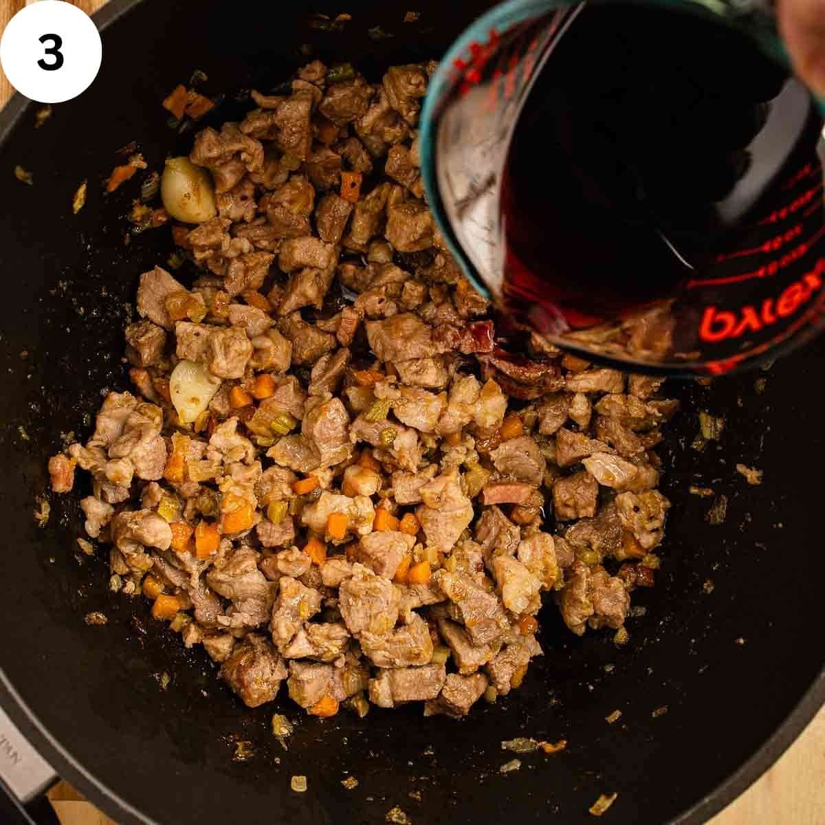 Adding red wine to chopped, cooked meat in a saucepan.