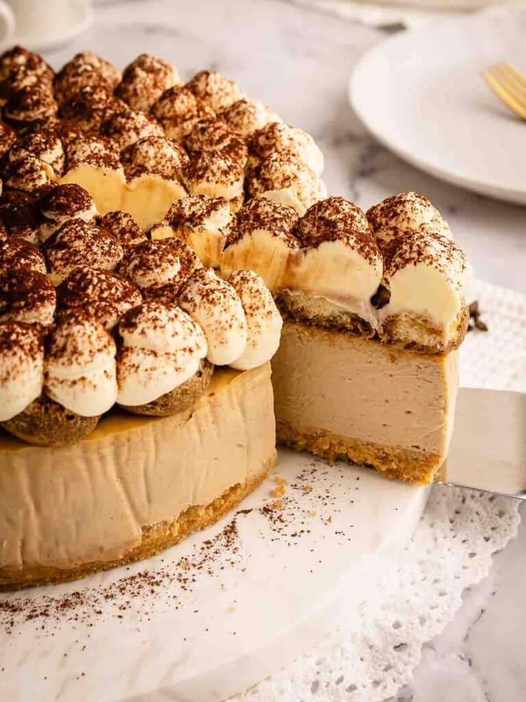 Baked tiramisu cheesecake with a slice cut and being removed on a cake server.
