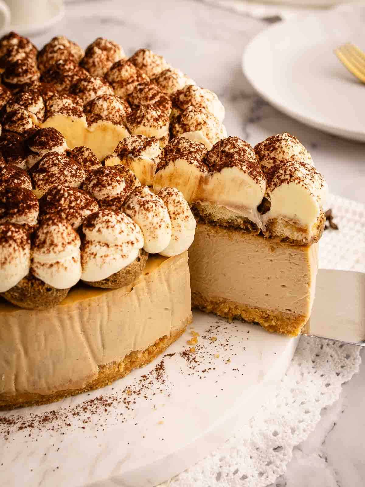 Baked tiramisu cheesecake with a slice cut and being removed on a cake server.