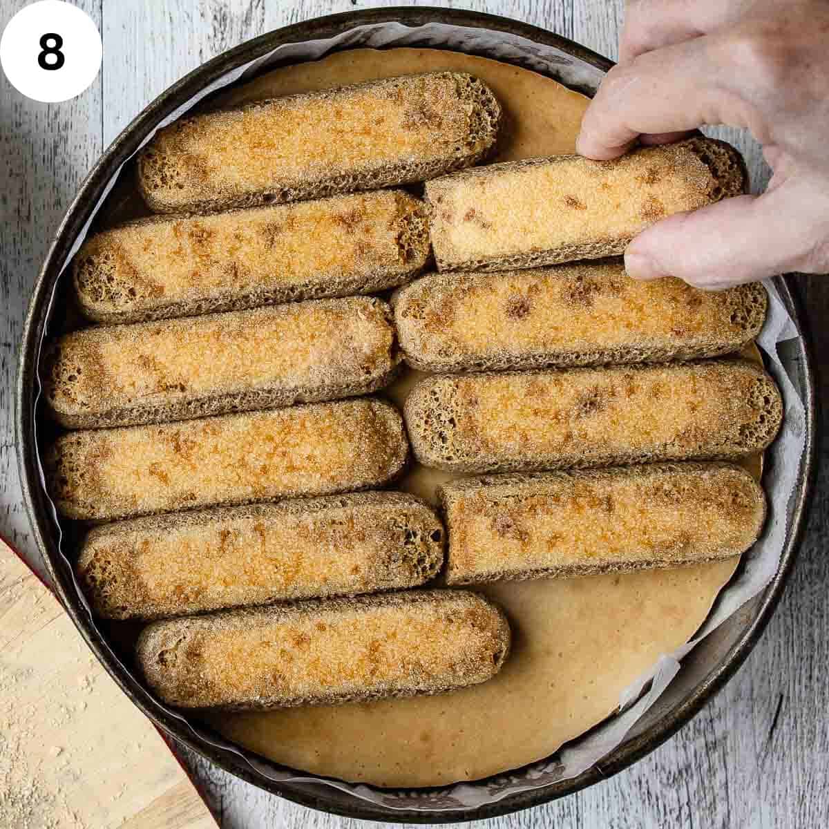 Adding coffee soaked savoiardi to the top of a baked cheesecake.