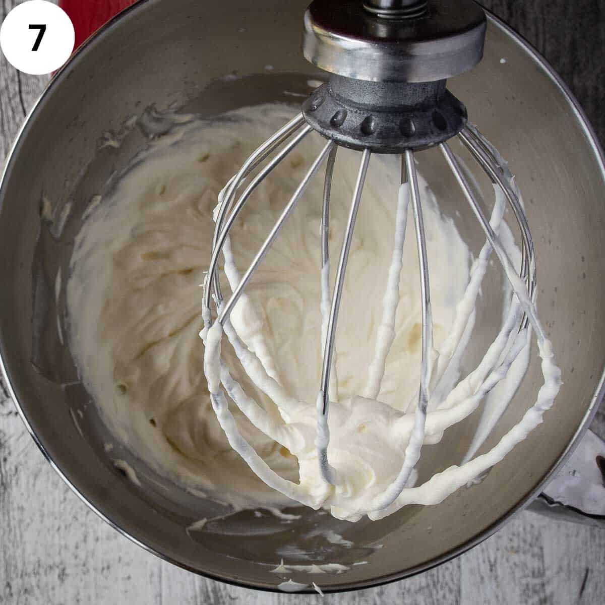 Whipped cream on the bowl of an electric mixer with the whisk lifted.