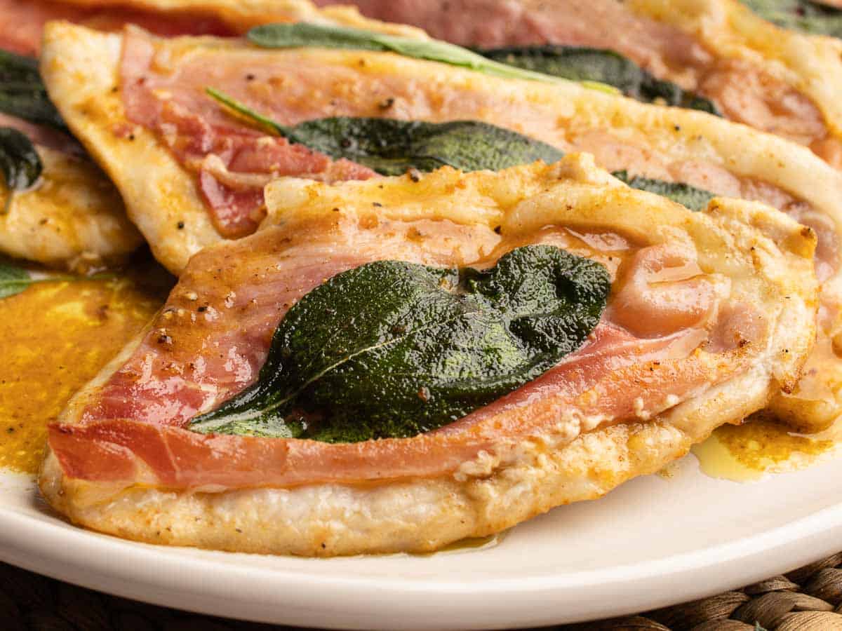 Close up of chicken cutlets topped with prosciutto and sage leaves.