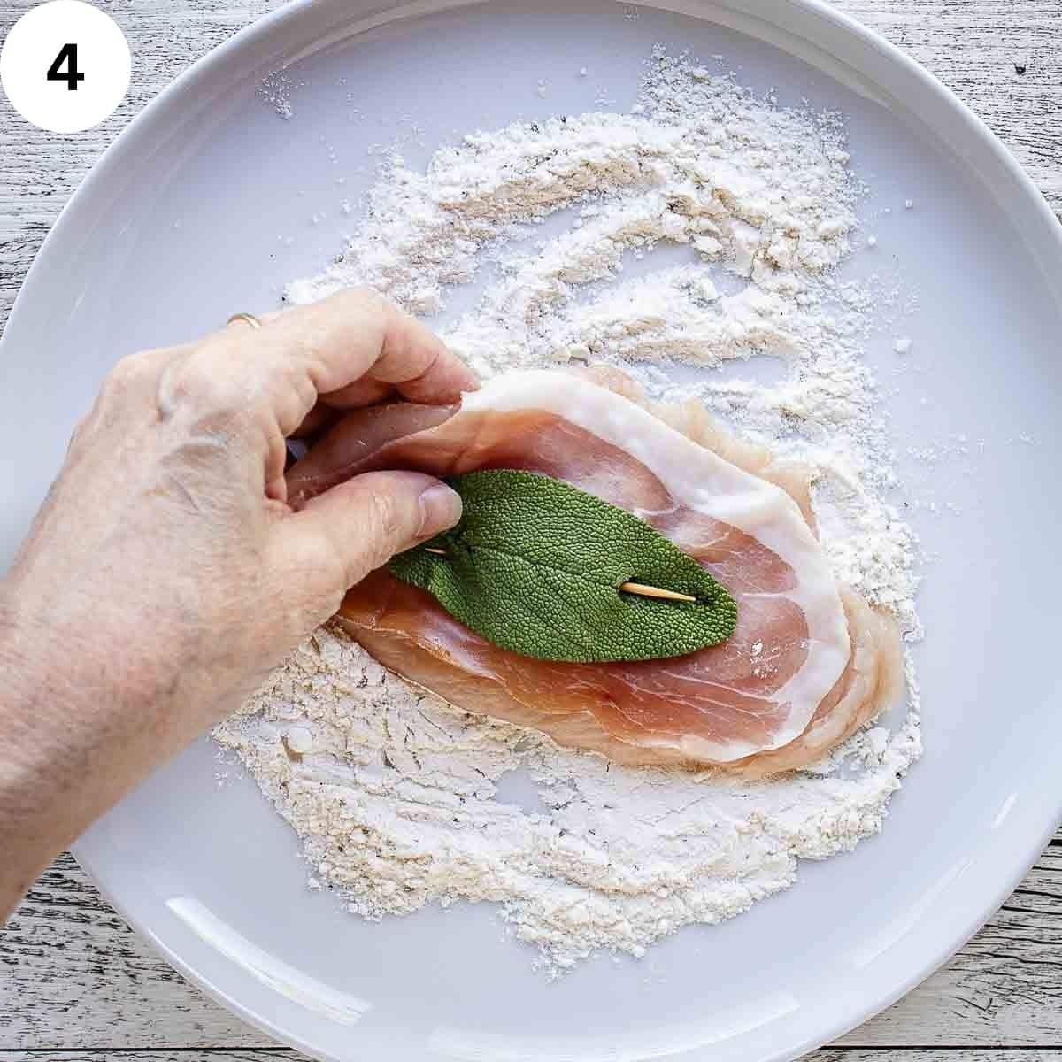 Flouring a chicken cutlet that has prosciutto and a sage leaf secured on with a toothpick.
