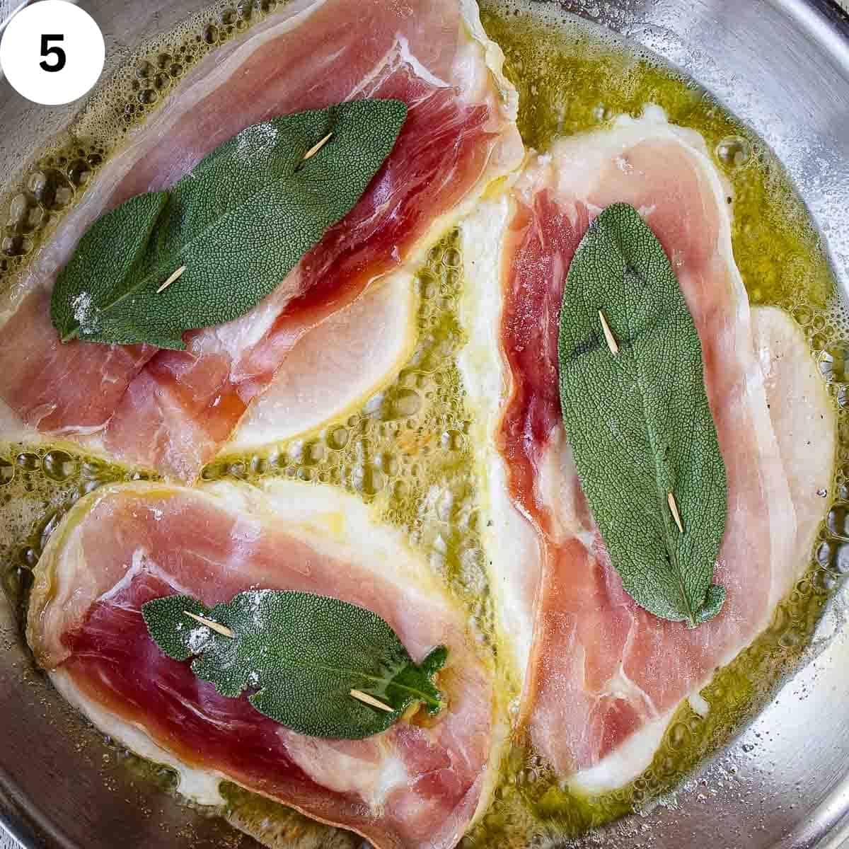 Three chicken cutlets with prosciutto and a sage leaf frying in a pan.