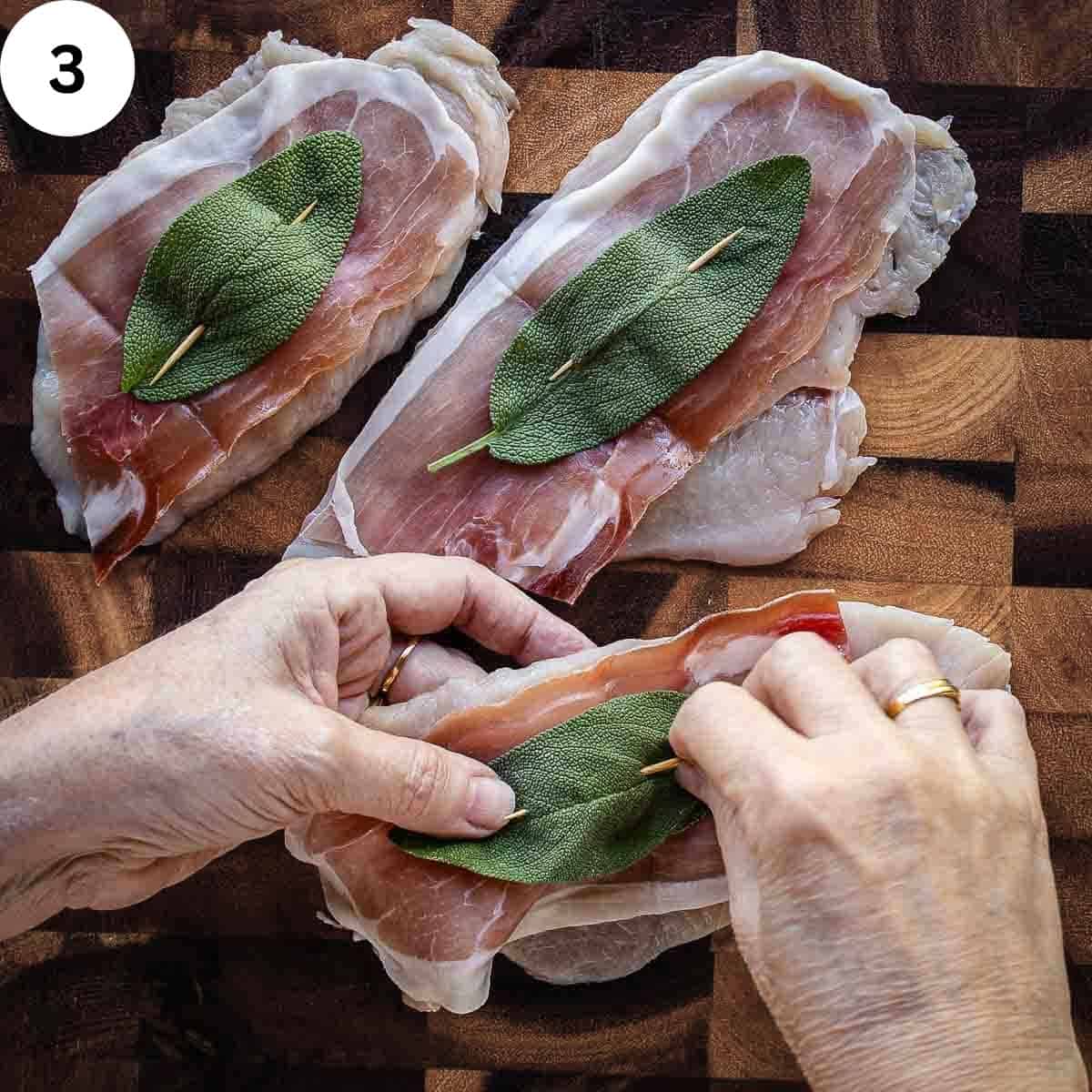 Skewering prosciutto and a sage leaf onto a chicken cutlet with a toothpick.