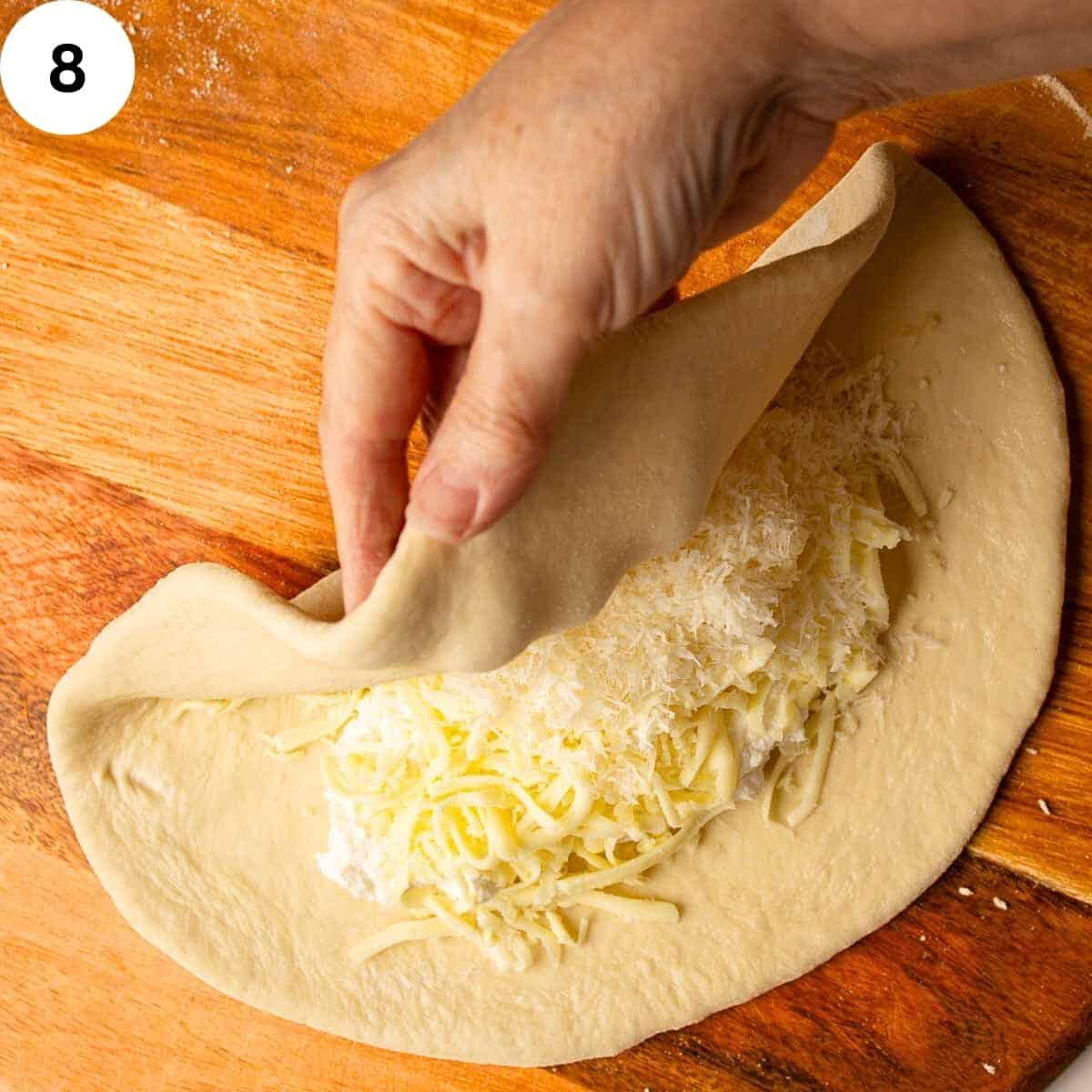Folding dough over shredded cheese filling to shape a calzone.
