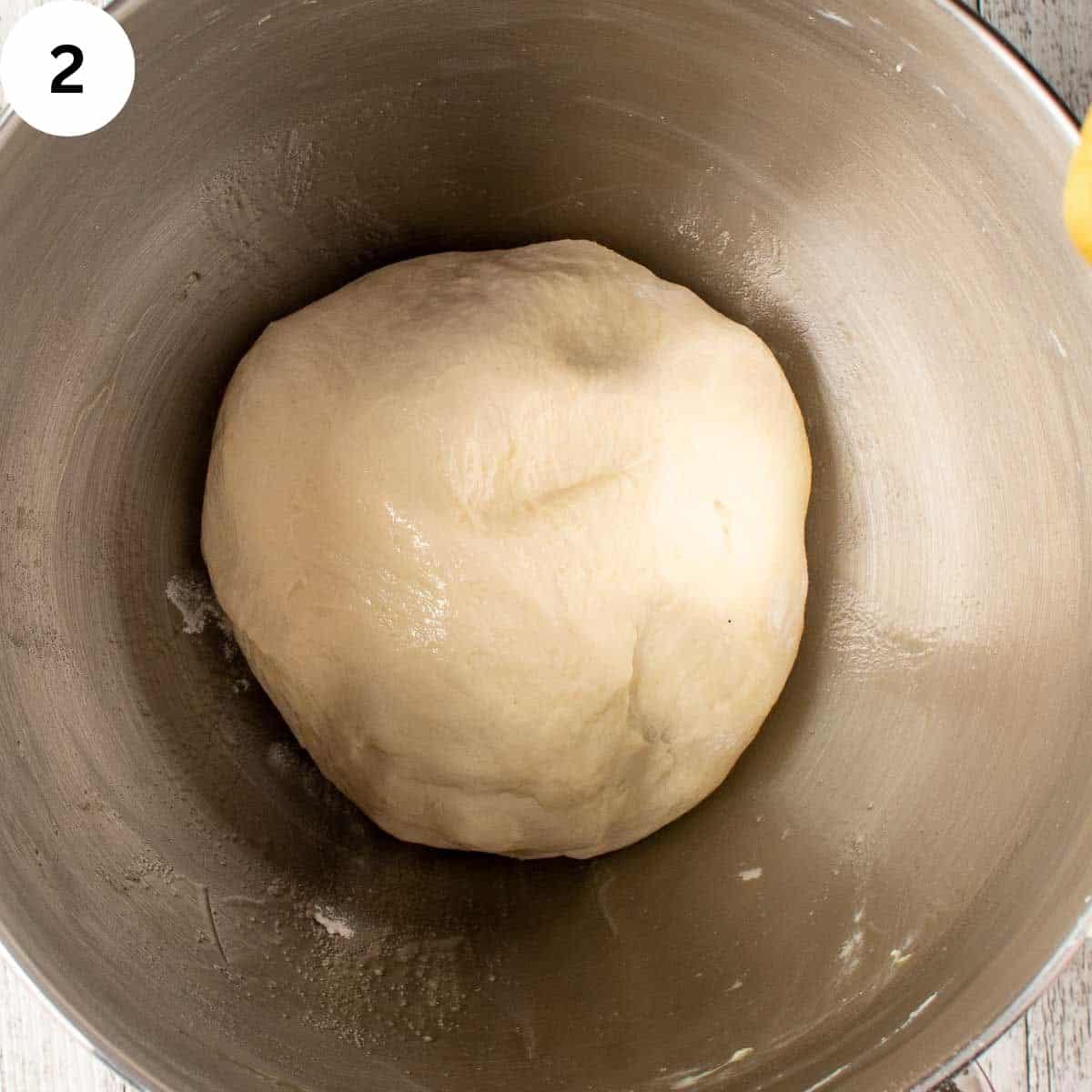 Smooth ball of kneaded dough resting in a metal mixing bowl before rising.