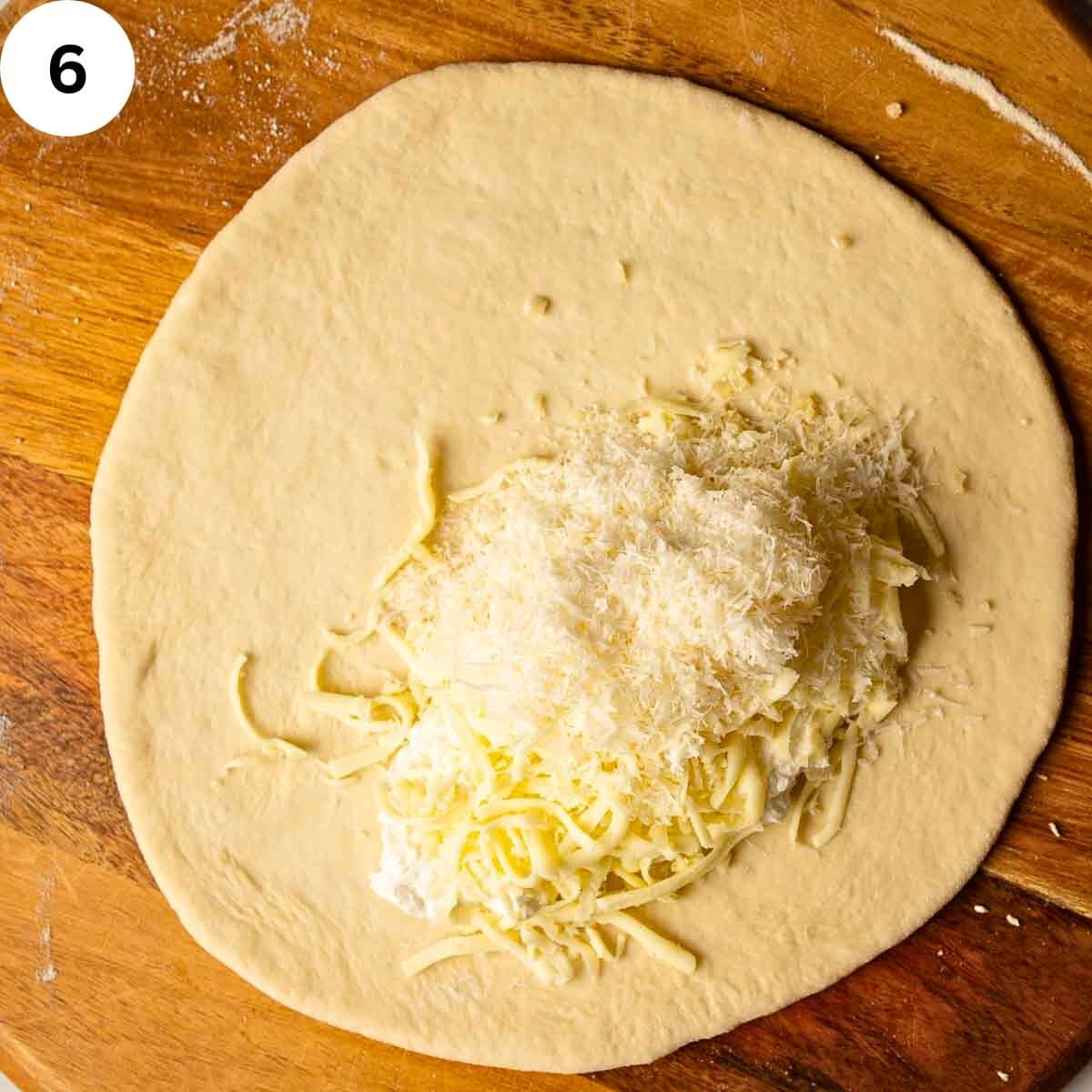 Shredded cheese piled in the center of rolled dough ready for filling a calzone.