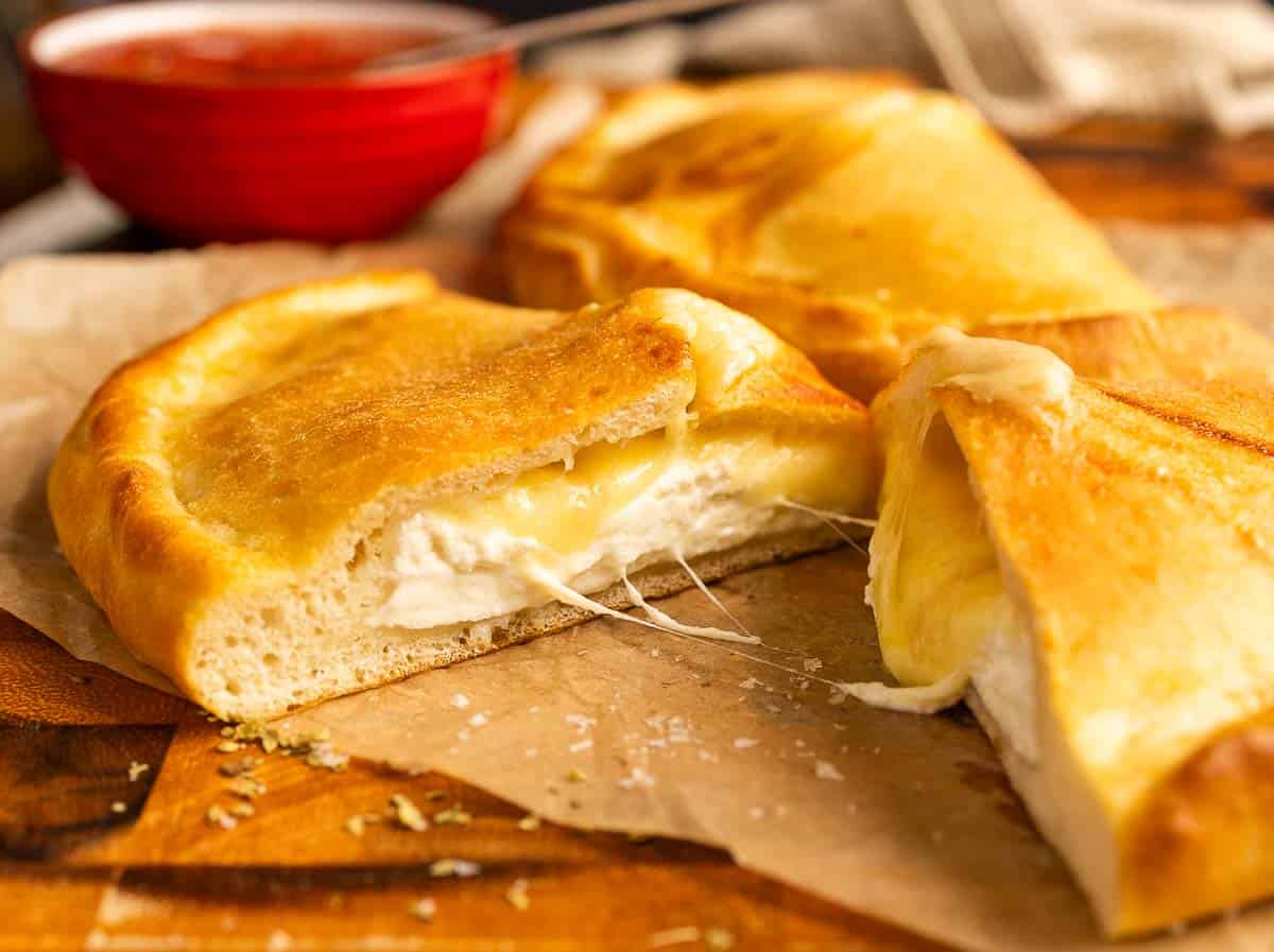 Cut baked calzone with melted mozzarella and ricotta filling on a wooden board.