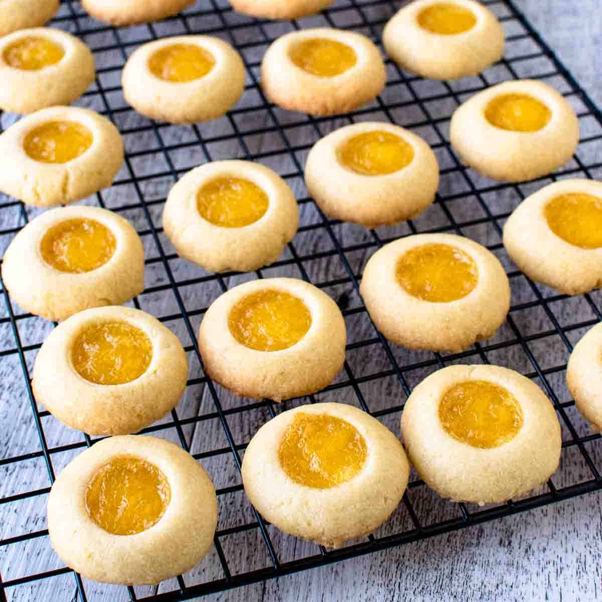 Rows of cookies with yellow centres on a black wire rack.