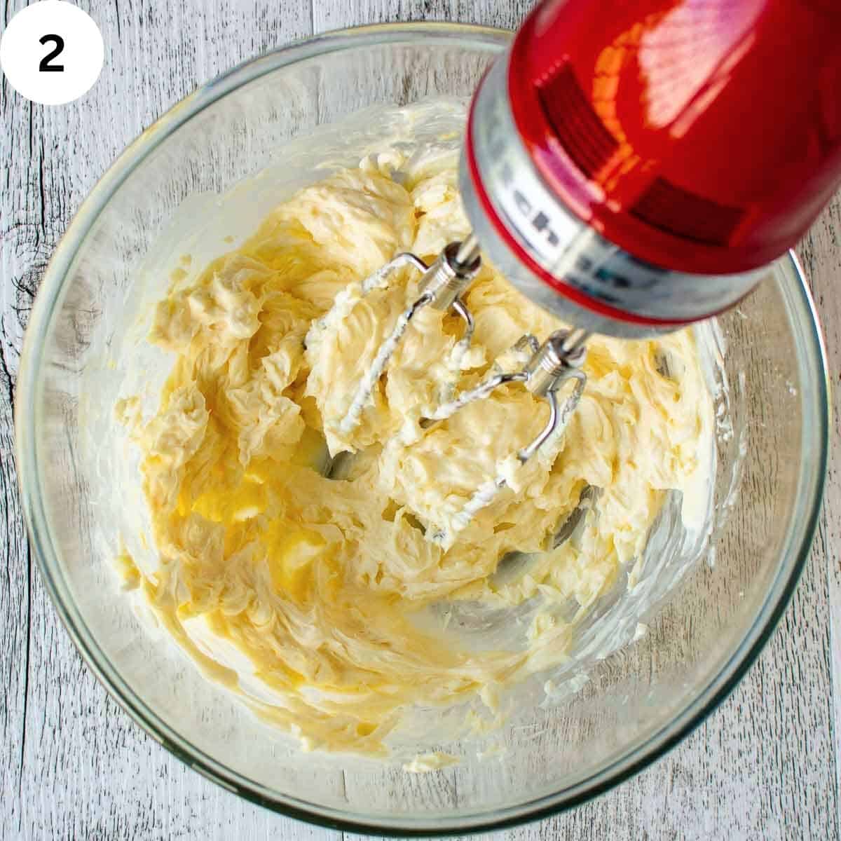Beating creamy mixture in a glass bowl with electric beaters.