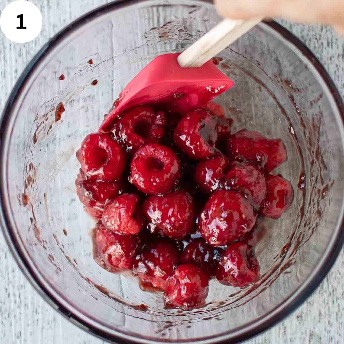 Stirring fresh raspberries with raspberry jam in a glass bowl.