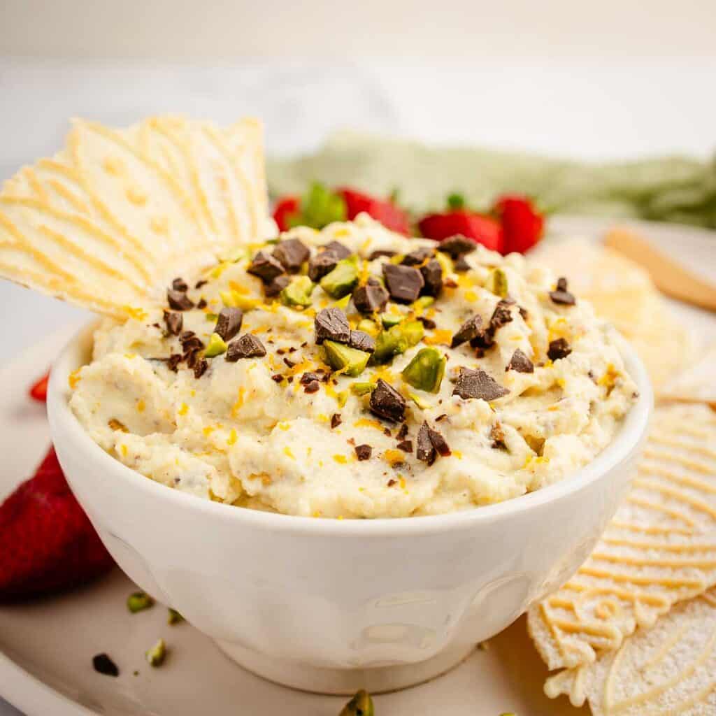 Creamy cannoli dip topped with chocolate chips and chopped pistachios and served with crispy pizzelle.