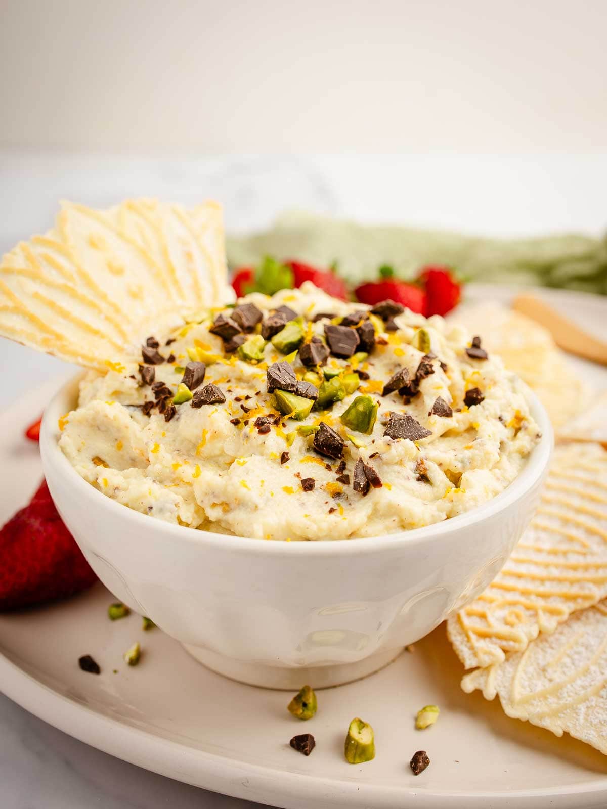 Creamy cannoli dip topped with chocolate chips and chopped pistachios and served with crispy pizzelle.