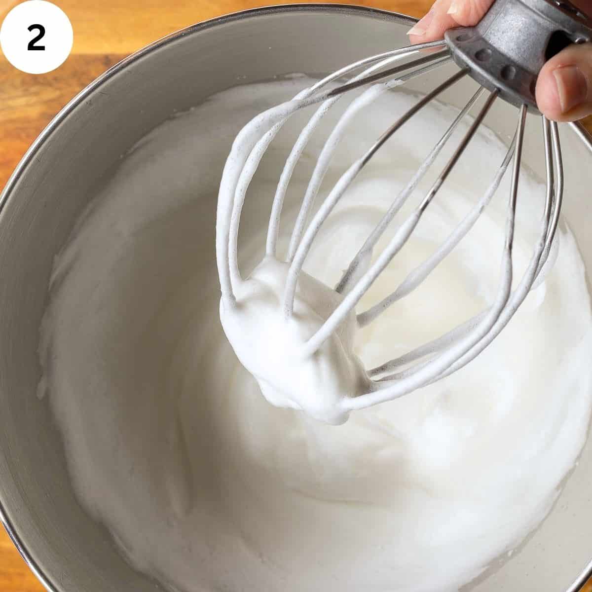 Firmly whipped egg whites in a stainless steel bowl.
