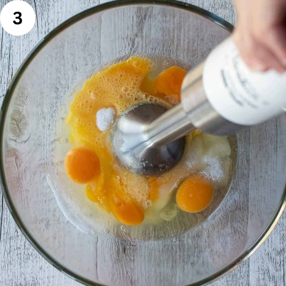 Eggs and sugar being whisked with an emersion blender.
