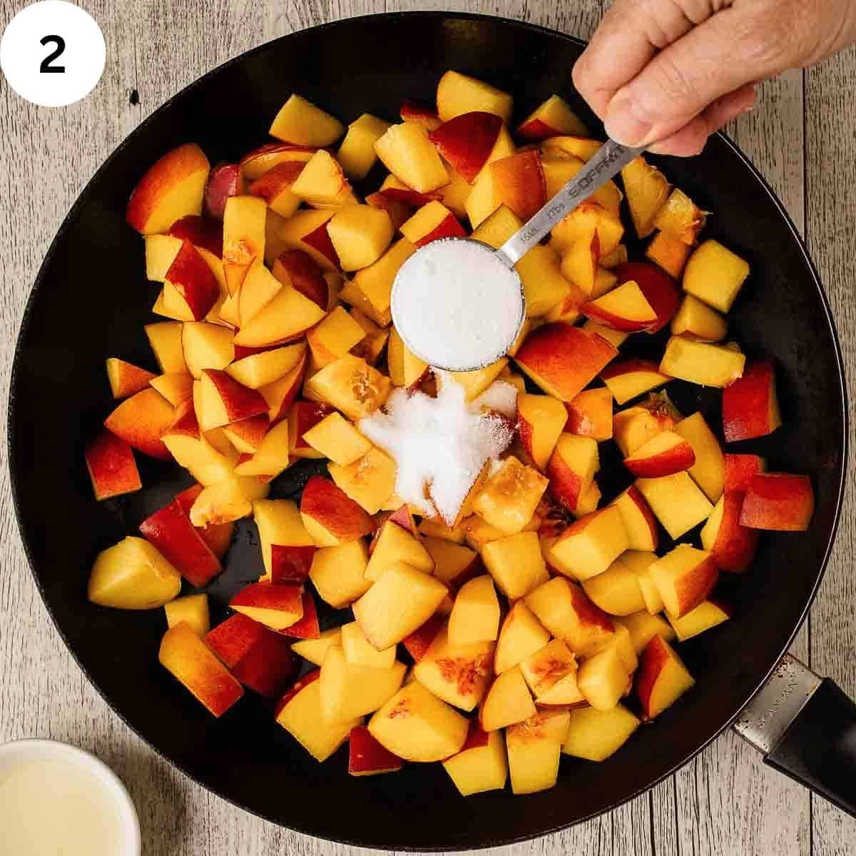 Adding white sugar to a skillet of chopped peaches.